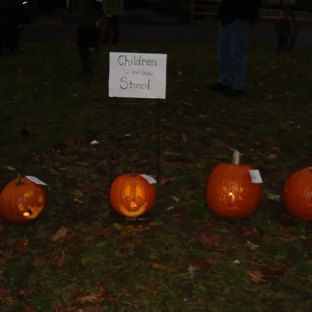 Four glowing pumpkins in front of the “Children 12 and Under Stencil” sign