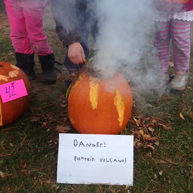 Smoke pouring from a pumpkin behind a sign that reads “Danger! Pumpkin Volcano!”